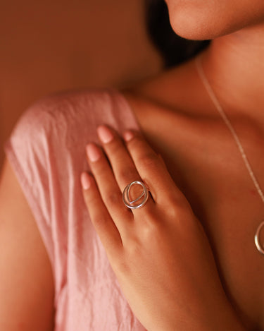 Close-up of a hand wearing Rosh silver sculptural ring with a blurred background